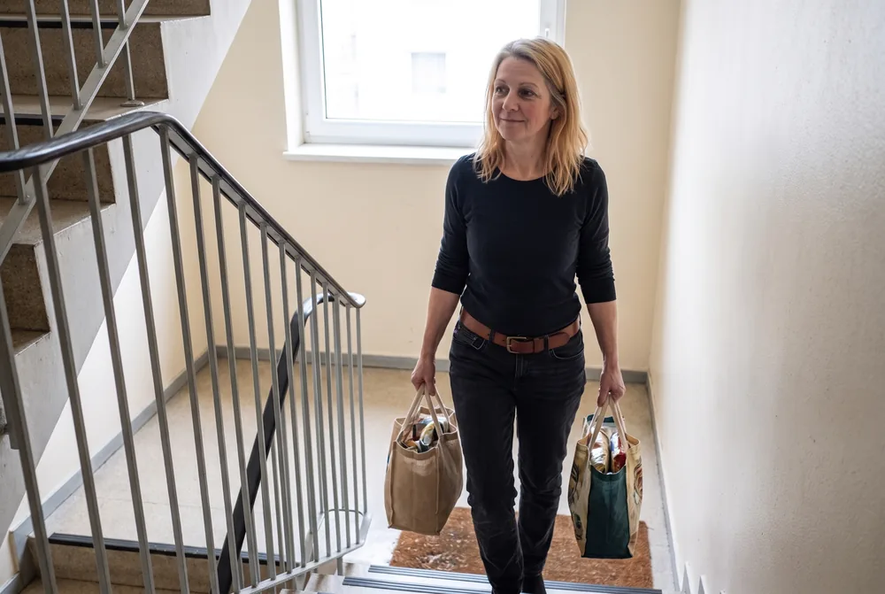 Frau trägt Einkaufstaschen die Treppe hinauf